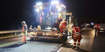 Travailleurs appliquant un nouvel enrobé sur la chaussée de nuit